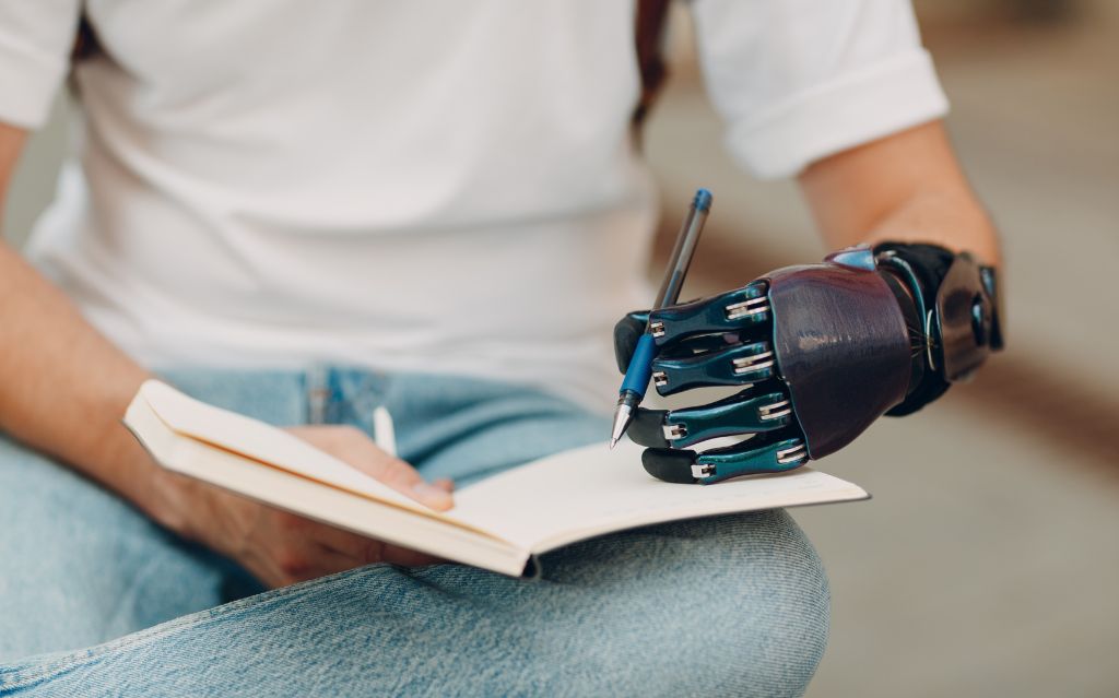 Ragazzo con jeans, maglia bianca e protesi al braccio che scrive su un quaderno