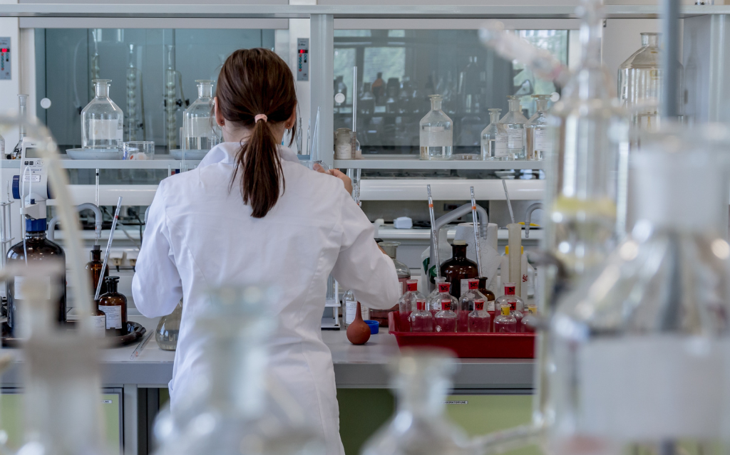 donna scienziata di spalle in un laboratorio pieno di provette e boccette di vetro